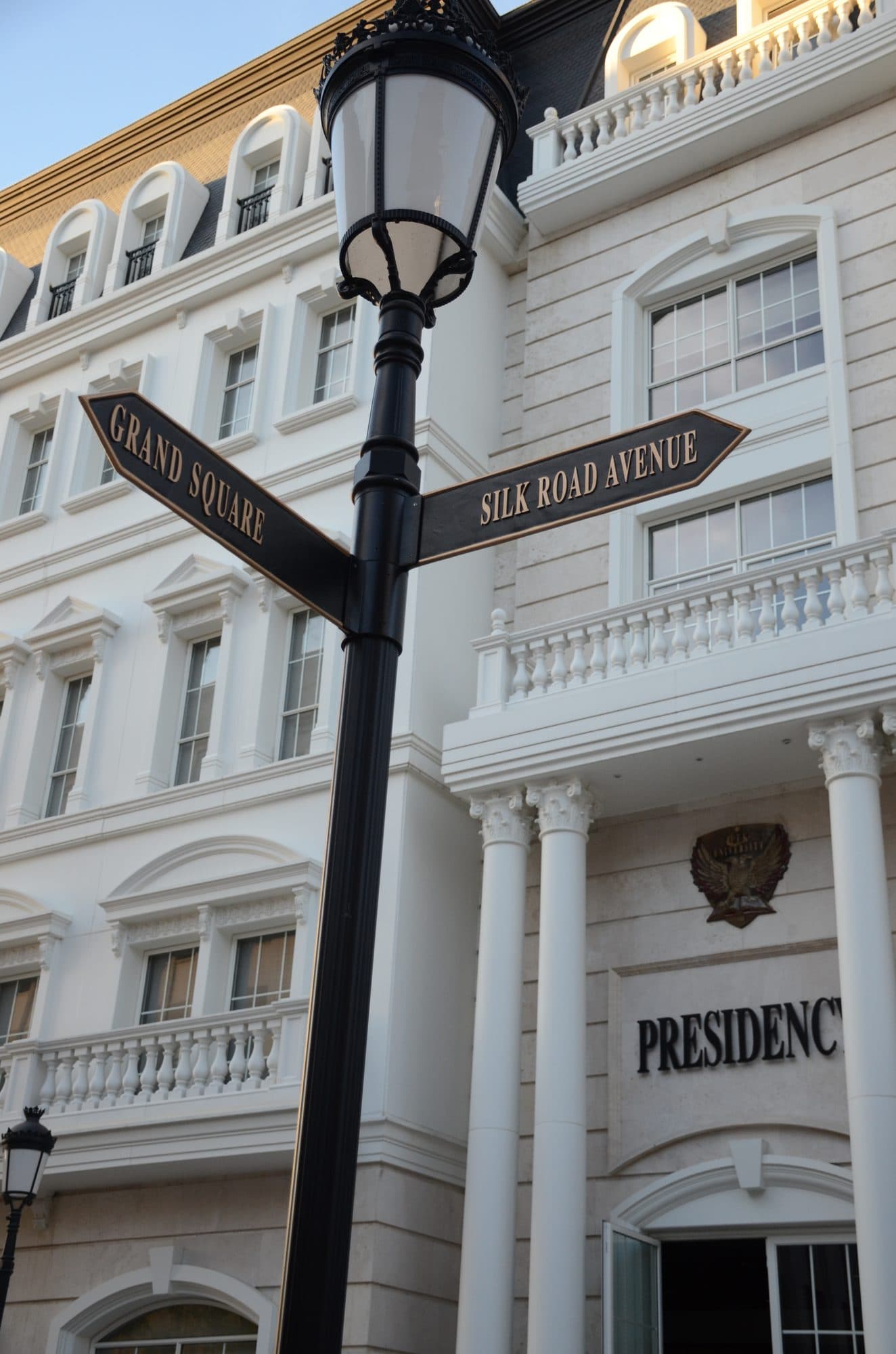 A campus lamp post marked Grand Square to the left and Silk Road Avenue to the right, with Presidency inscribed on the building behind.