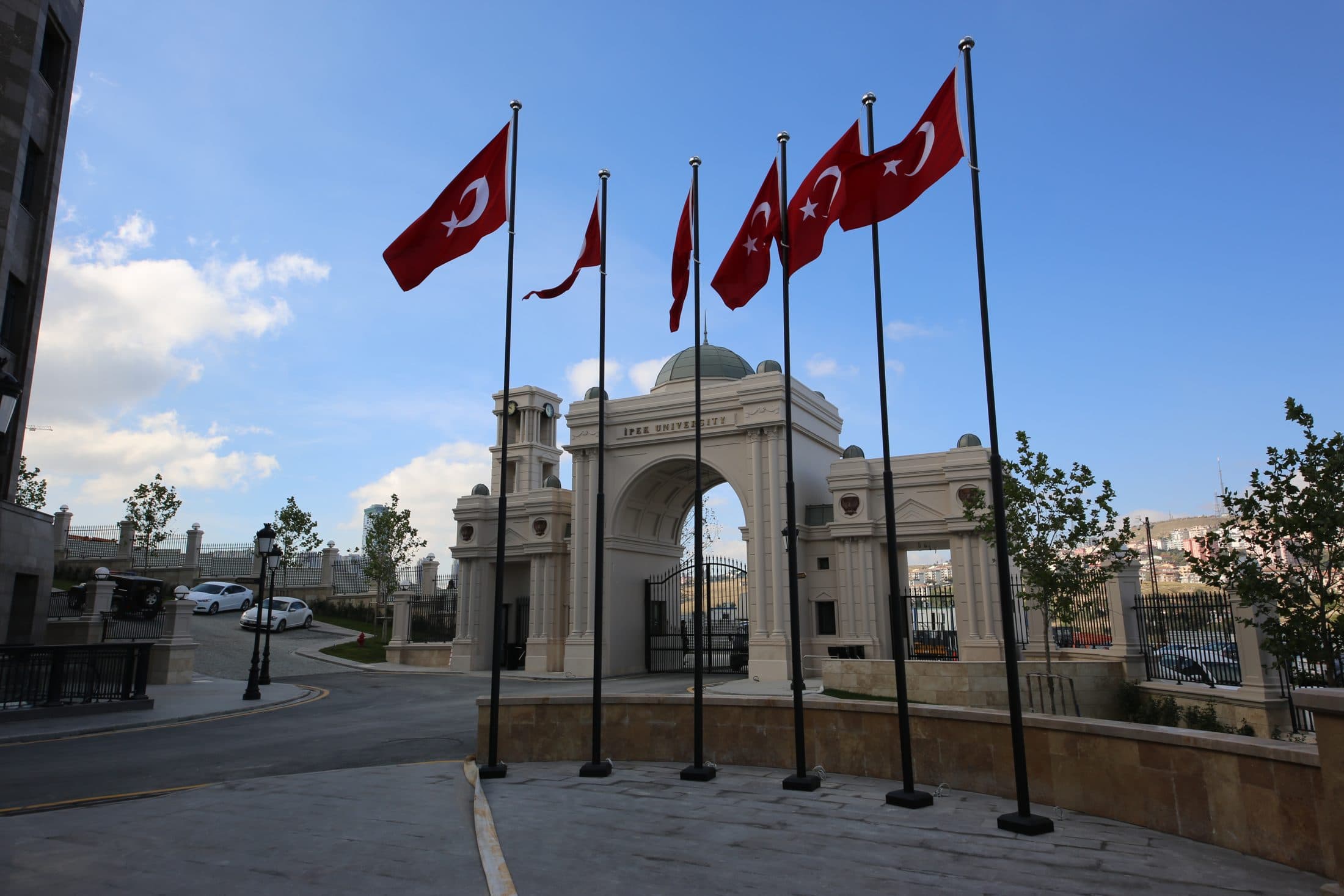 A white stone entrance arch inscribed İpek Üniversitesi, with Turkish flags in front.