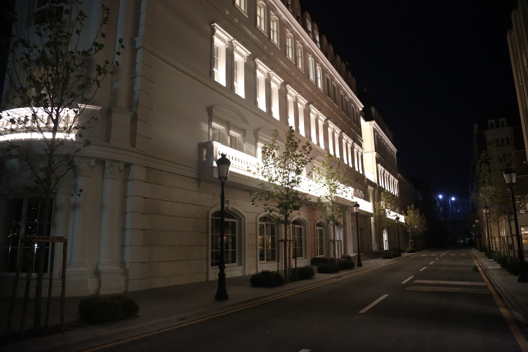 A night view of a campus building and street, with rounded columns and a balcony balustrade.
