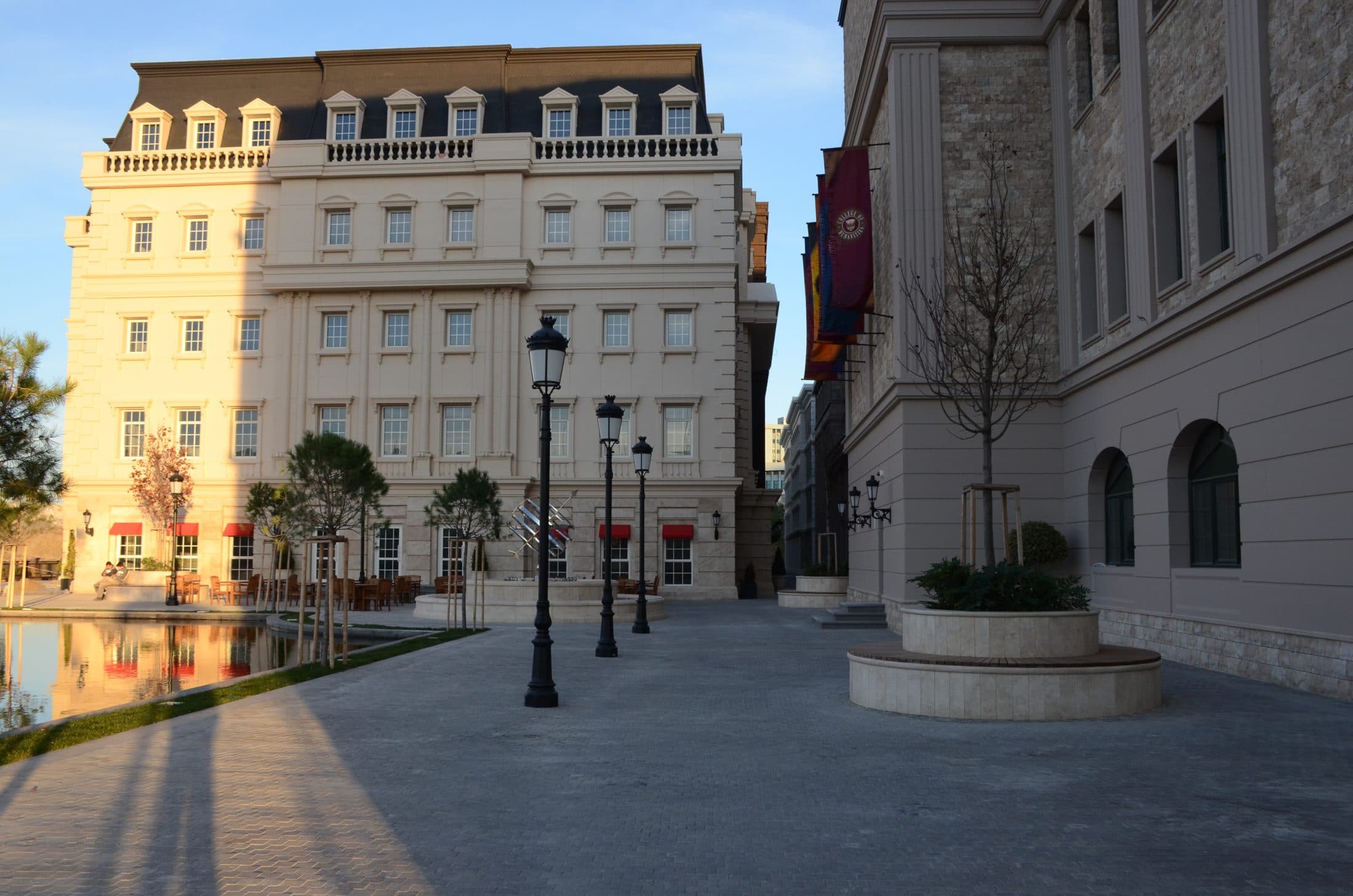 A campus plaza with still water to the left and university buildings to the right.
