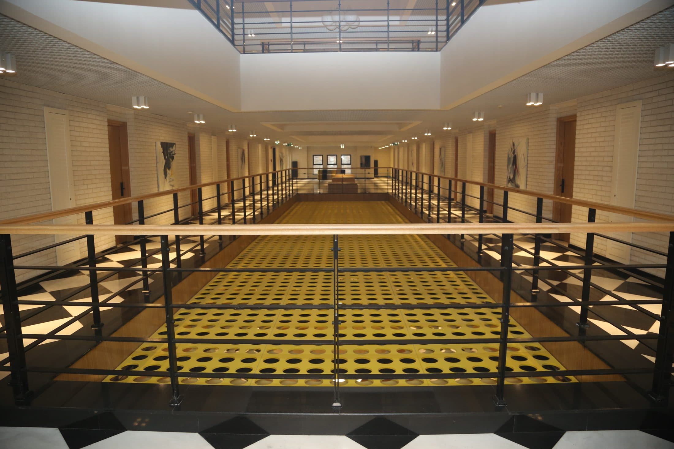 An interior corridor with a gallery opening and geometric floor, with no people in view.