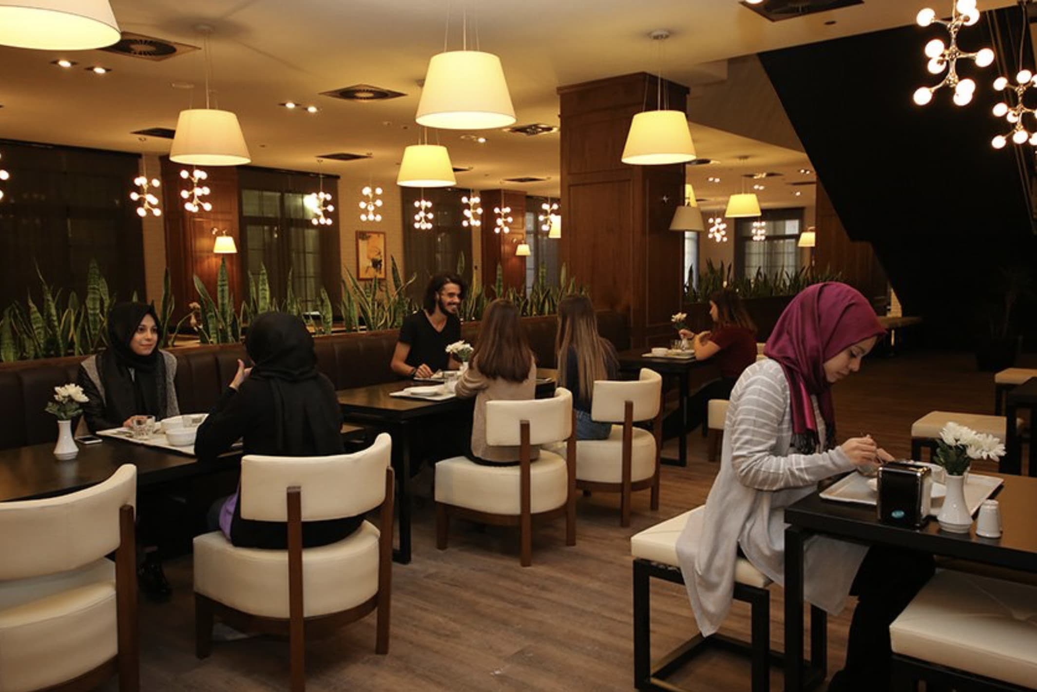 Students seated at tables in a dining area with conical pendant lamps.