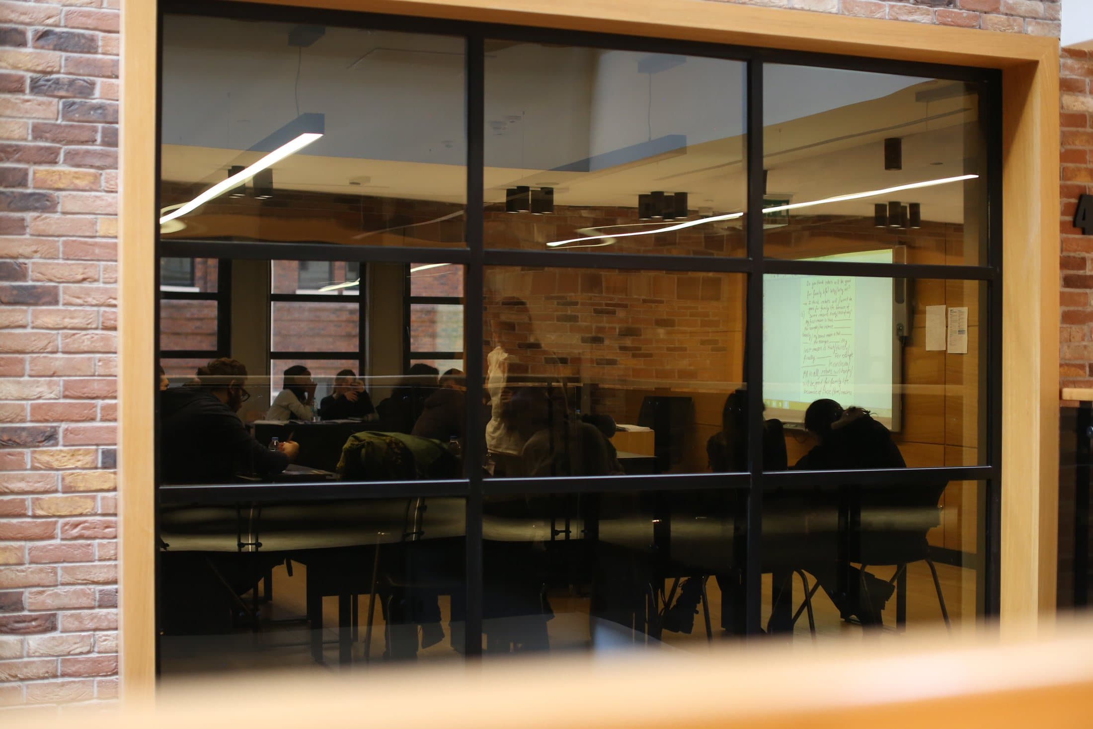 A study room seen through a wooden-framed window, with students seated at tables.
