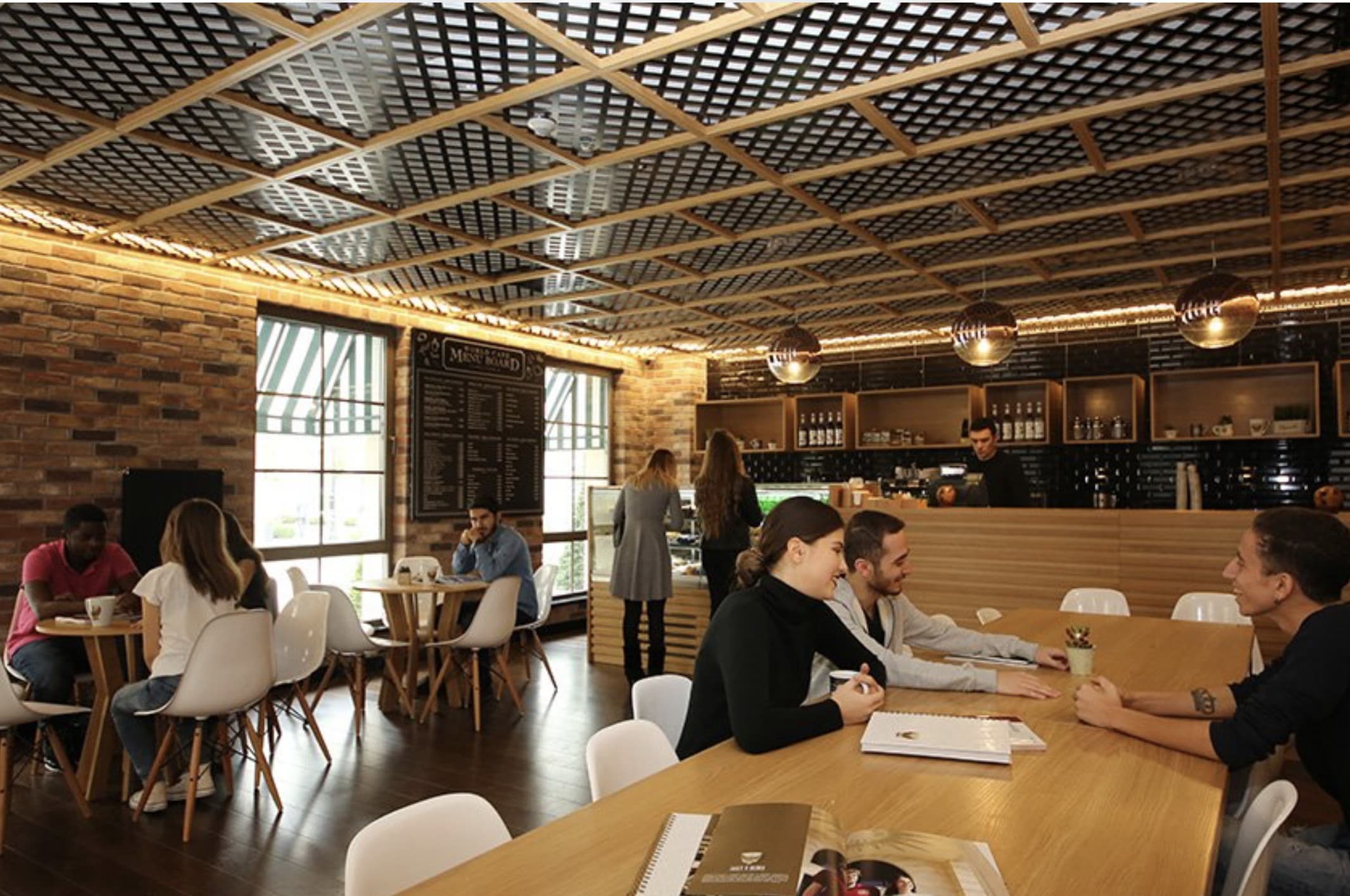 Students seated at wooden tables in a brick-walled café interior.